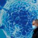 A man wearing a protective face mask walks past an illustration of a virus, August 3, 2020.