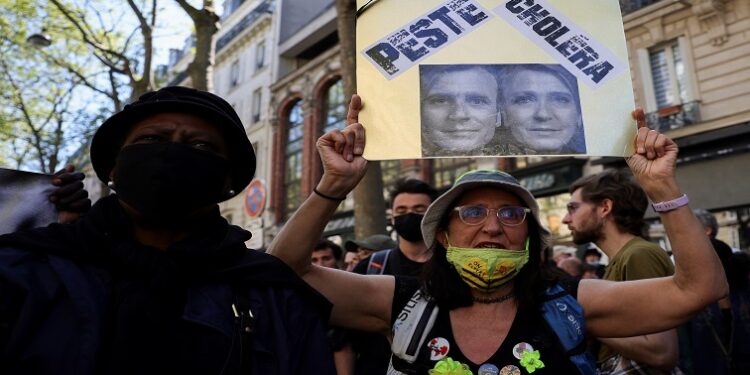 A member of the Yellow Vests movement holds a placard with the words "Pest" and "Cholera" with pictures of French President Emmanuel Macron and far-right presidential candidate Marine Le Pen, during a demonstration against far-right, racism and fascism ahead of the second round of the 2022 presidential election, in Paris, France, April 16, 2022.