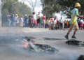 [FILE IMAGE] Residents are seen in the background as tyres burn on the streets.