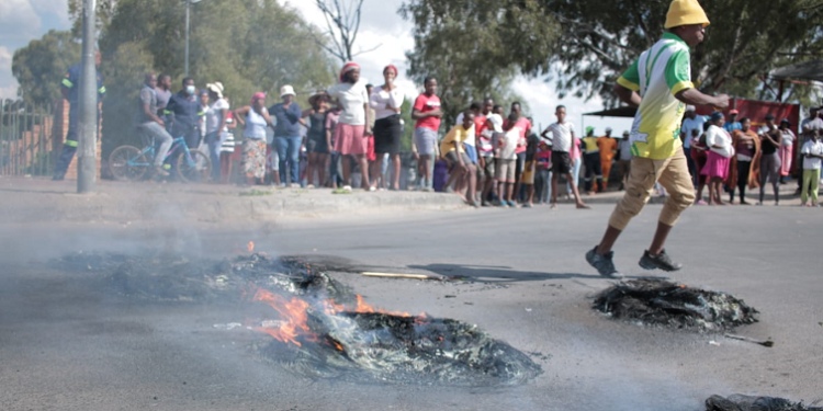 Diepsloot residents are seen in the background as tyres burn on the streets of the township located north of Johannesburg, where residents are protesting against rampant crime in the area