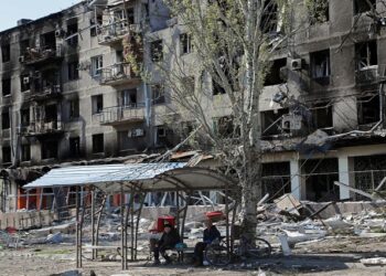 Local residents sit on a bench near an apartment building damaged during Ukraine-Russia conflict in the southern port city of Mariupol, Ukraine April 28, 2022.