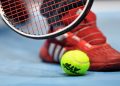 Tennis racquet and ball seen next to a player's shoe
