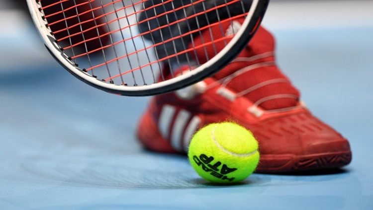 Tennis racquet and ball seen next to a player's shoe