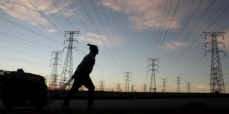 A man pulls a trolley as he walks past electricity pylons in South Africa.