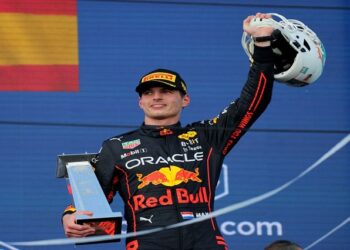 Red Bull's Max Verstappen celebrates on the podium after winning the Miami Grand Prix with the Miami Dolphin's helmet.