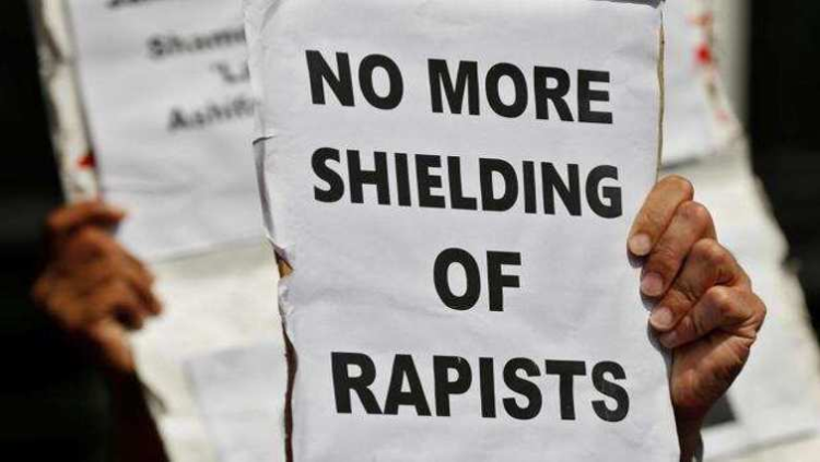 A person holds up a sign against the shielding of rapists