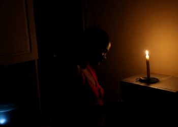 A lady stands in front of the candle in the kitchen.