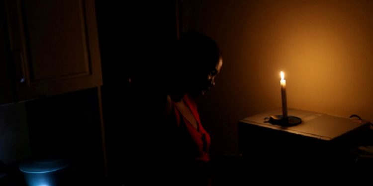 A lady stands in front of the candle in the kitchen.