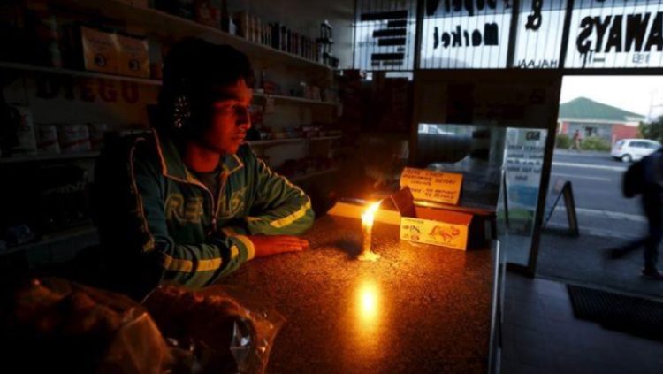A shopkeeper waits for customers in his candlelit fast food store during a load shedding electricity blackout in Cape Town April 15, 2015.