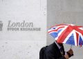 FILE PHOTO: A worker shelters from the rain under a Union Flag umbrella as he passes the London Stock Exchange in London, Britain