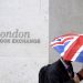 FILE PHOTO: A worker shelters from the rain under a Union Flag umbrella as he passes the London Stock Exchange in London, Britain