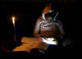 Thandiwe Sithole looks at her mobile phone as she studies by a candle light during one of frequent power outages from South African utility Eskom caused by its aging coal-fired plants, in Soweto, South Africa March 9, 2022.