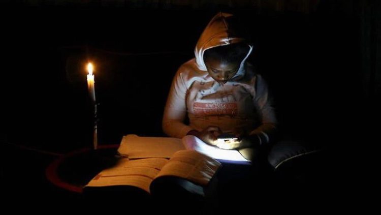 Thandiwe Sithole looks at her mobile phone as she studies by a candle light during one of frequent power outages from South African utility Eskom caused by its aging coal-fired plants, in Soweto, South Africa March 9, 2022.
