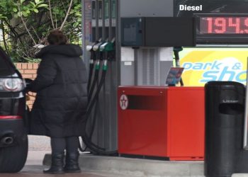 A woman fills up her car in front of a sign showing increased fuel prices at a filling station near Liverpool, Britain, March 10, 2022.