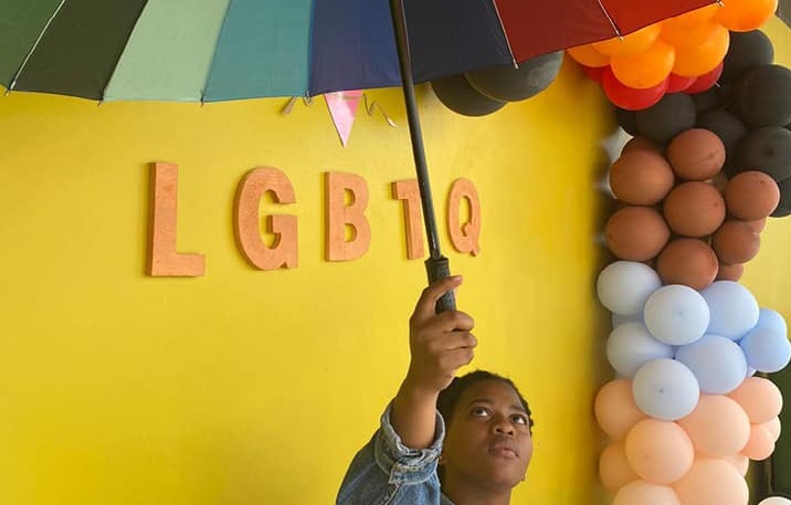 A person holds an umbrella over a LGBTQ sign, Nov 2021