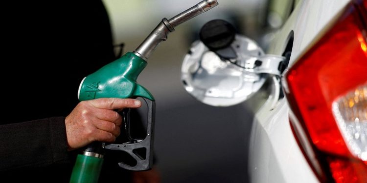 A man holds a fuel nozzle at a petrol station.