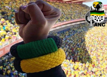 A person holds up a fist with ANC colours on an armband