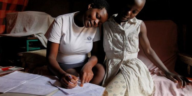 A pregnant teenager sits next to her friend as she completes her school work