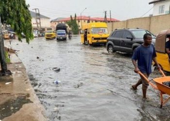 A man wades through flood water with his wheel barrow, after rainfall with some objects seen floating in the flood water in Lagos, Nigeria.