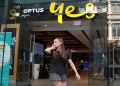 A woman uses her mobile phone as she walks past in front of an Optus shop in Sydney, Australia, February 8, 2018.