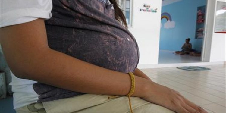 An unnamed 18-year-old teenager, who is eight months pregnant, rests outside her room.