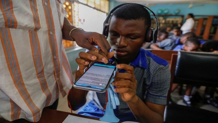 A Vinsighte team member assists a visually impaired student with the Visis app, which aims at helping him read, at Pacelli School for the Blind and Partially Sighted Children, in Lagos, Nigeria, October 12, 2022.