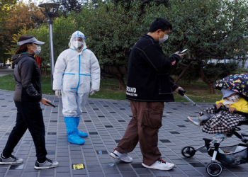 A pandemic prevention worker wears a protective suit as people line up to get swab tests at a testing booth as outbreaks of coronavirus disease continue in Beijing, China, November 3, 2022