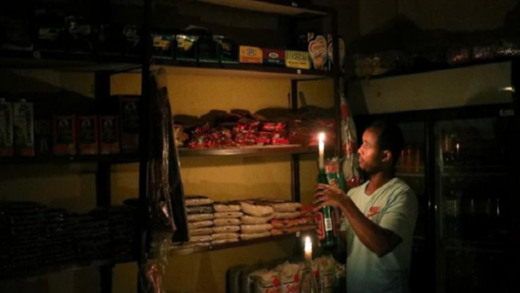 Mulugeta Desalegn, an owner of a convenience store, or "spaza shop", picks an item for a customer as he holds a candle, in Senaone, Soweto, South Africa March 18, 2019.
