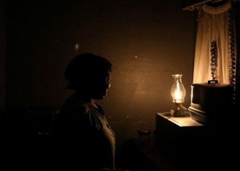 [File Image] : A women looks on next to a parafin light during an electricity load-shedding blackout in Soweto