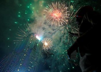 A reveller looks at fireworks explode over a building during the New Year's Eve celebrations.