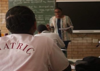 A learner wearing a  T- shirt written ''Matric'' is seated in a classroom.