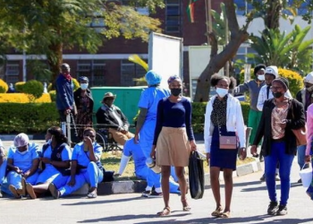 People walk past Zimbabwean medical workers as they sit outside Sally Mugabe Hospital during a strike by state doctors and nurses to press for higher pay, in Harare, Zimbabwe.