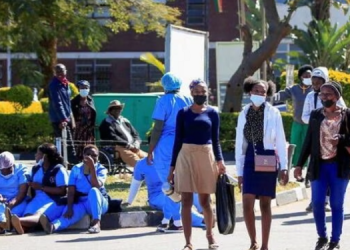 File image: People walk past Zimbabwean medical workers as they sit outside Sally Mugabe Hospital during a strike by state doctors and nurses to press for higher pay, in Harare, Zimbabwe.