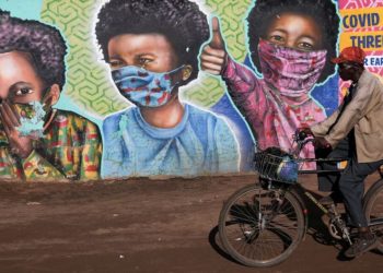 A man rides his bike past a mural by Senzart911 that shows people wearing facemasks