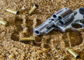 A gun and bullets on the sand.
