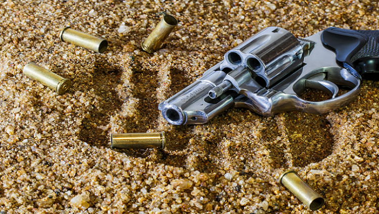 A gun and bullets on the sand.