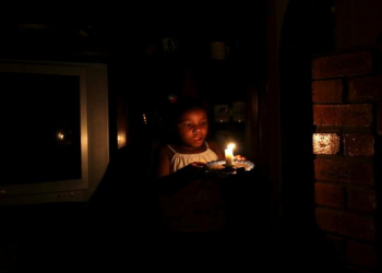 A child walking while holding a candle during the rolling blackouts.