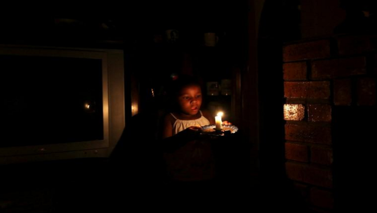 A child walking while holding a candle during the rolling blackouts.