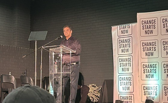 Jardine standing at the podium with party banner behind him.